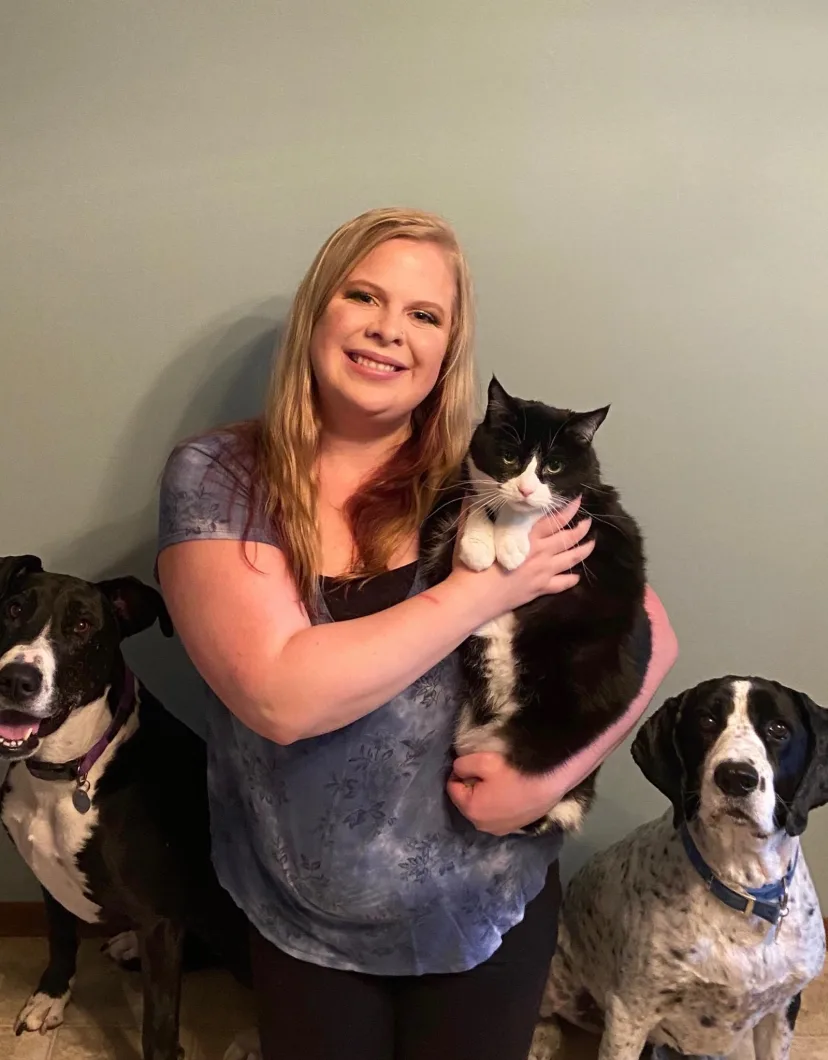 Abby's staff photo from Heather Ridge Pet Hospital where she is holding her black and white cat with her two black and white dogs on each side of her.
